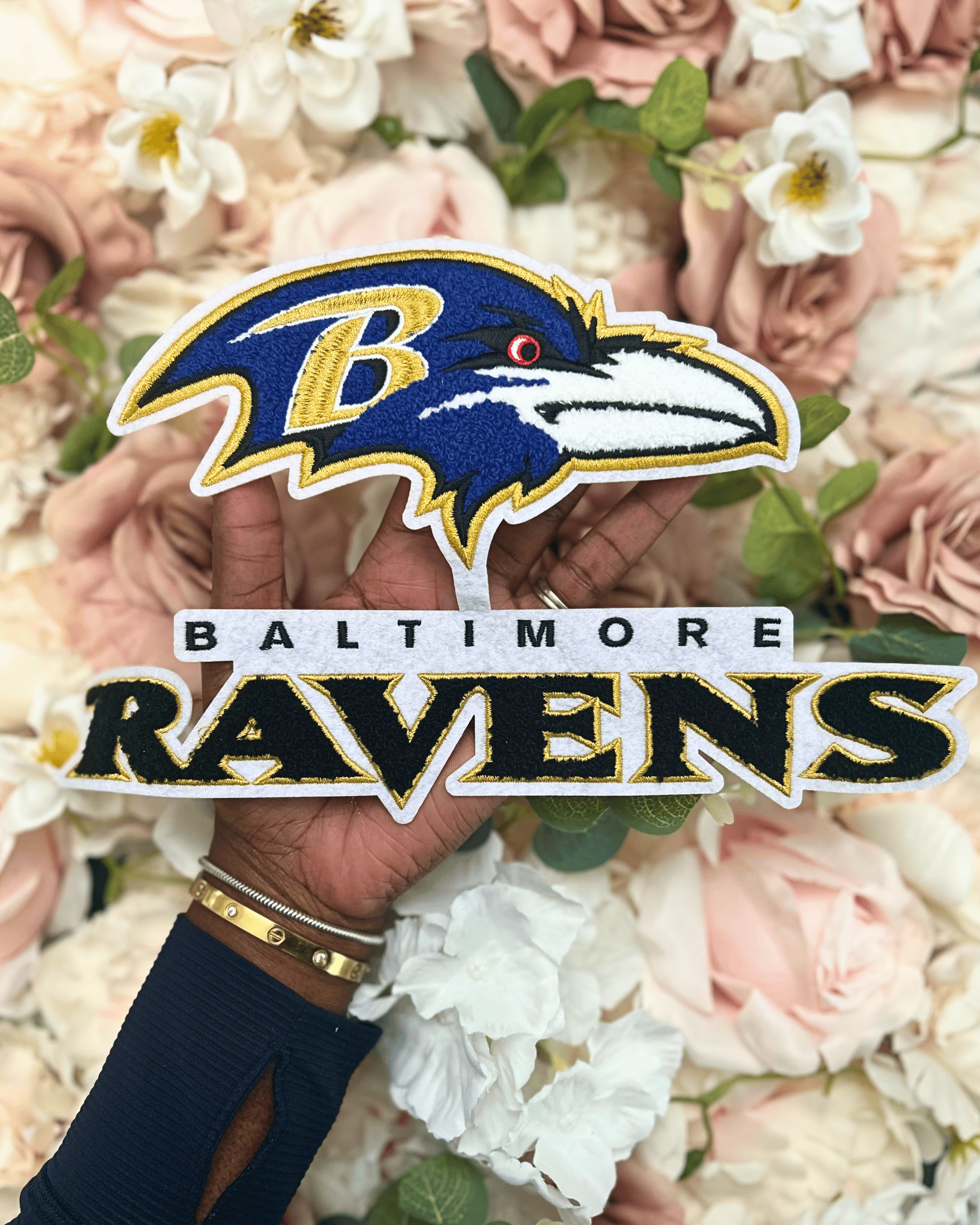 Baltimore Ravens logo with a hand holding it against a floral background