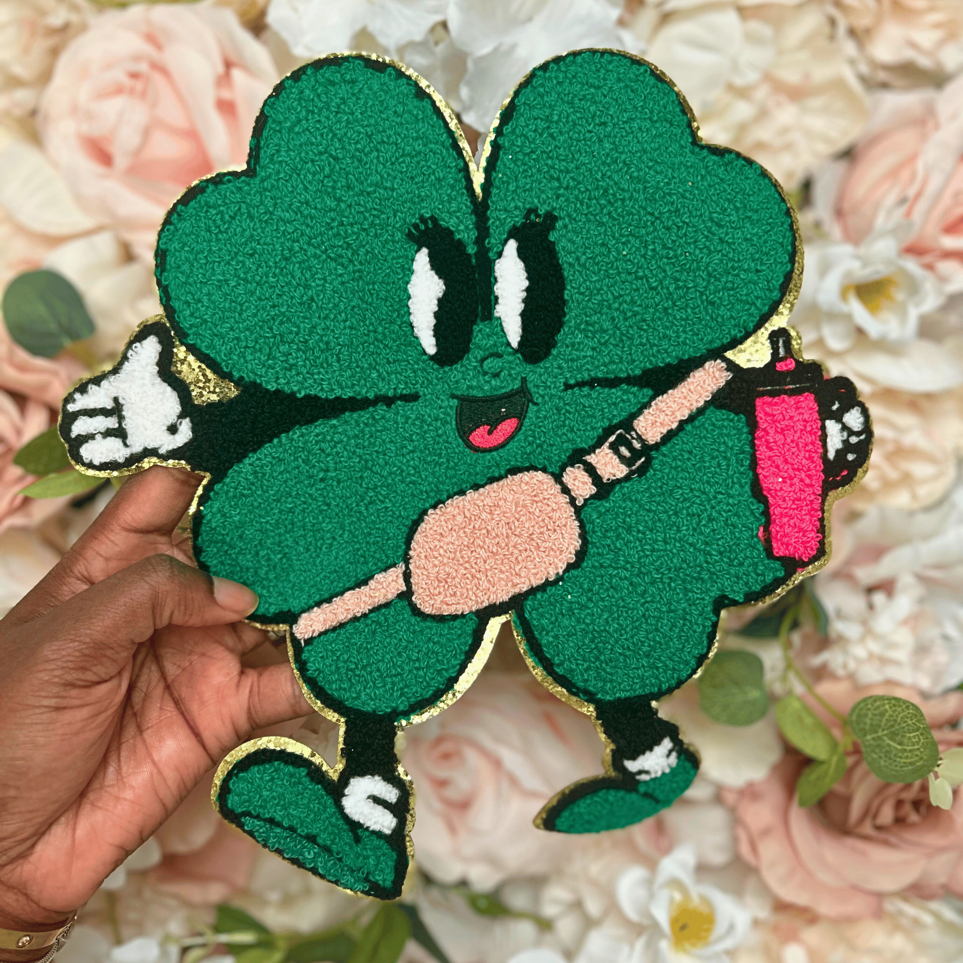 Green cartoon character patch held over a floral background