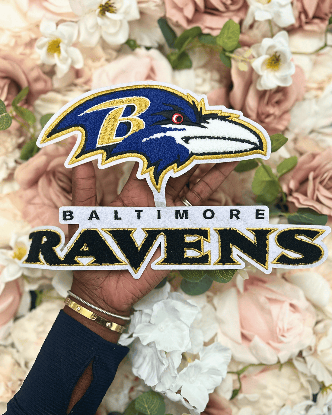 Baltimore Ravens logo with a hand holding it against a floral background