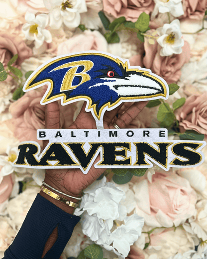 Baltimore Ravens logo with a hand holding it against a floral background