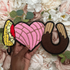 Three colorful patches shaped like a corn, pink heart, and brown donut held over a floral background.