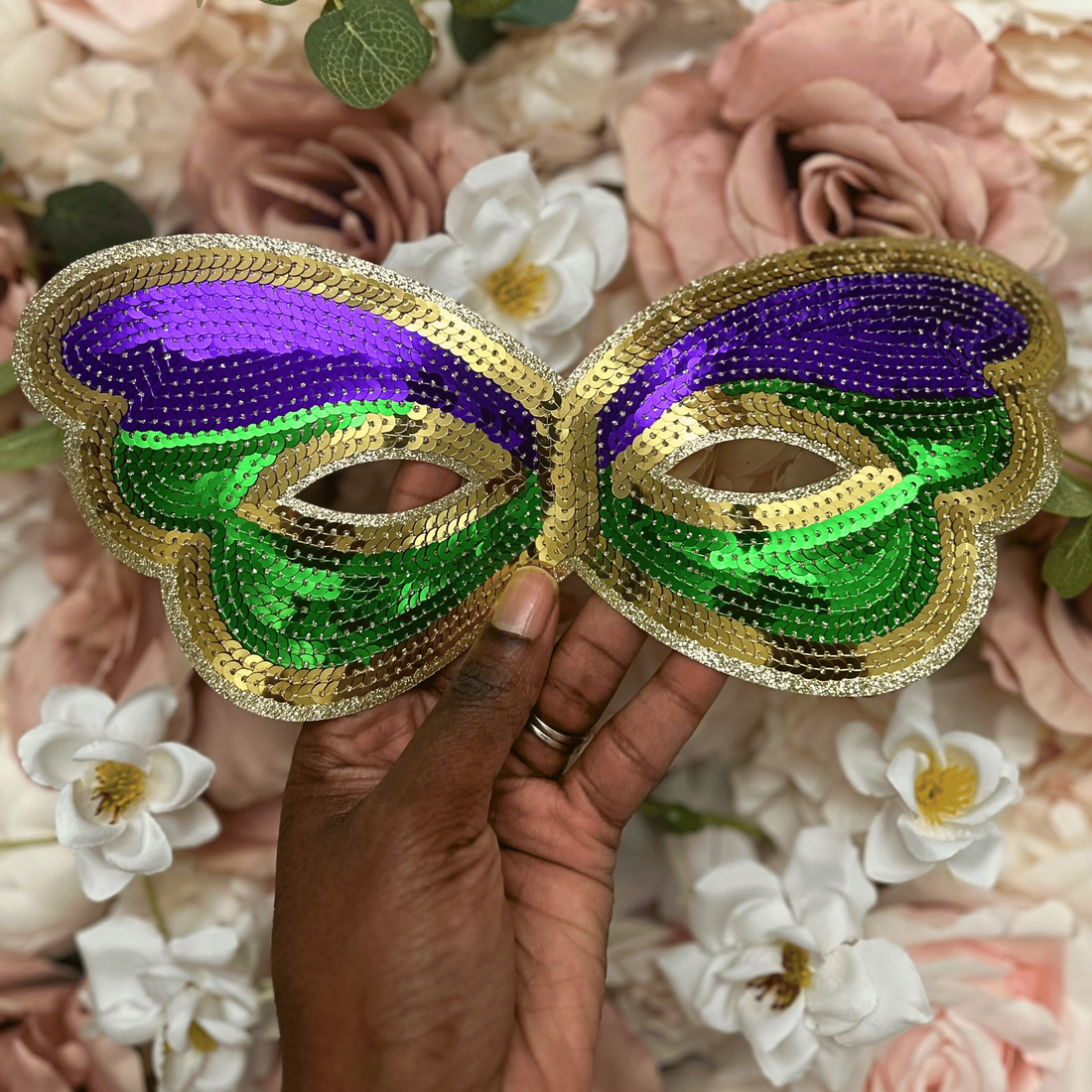 Mardi Gras masks with purple, green, and gold held in front of a floral background