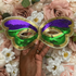 Mardi Gras masks with purple, green, and gold held in front of a floral background