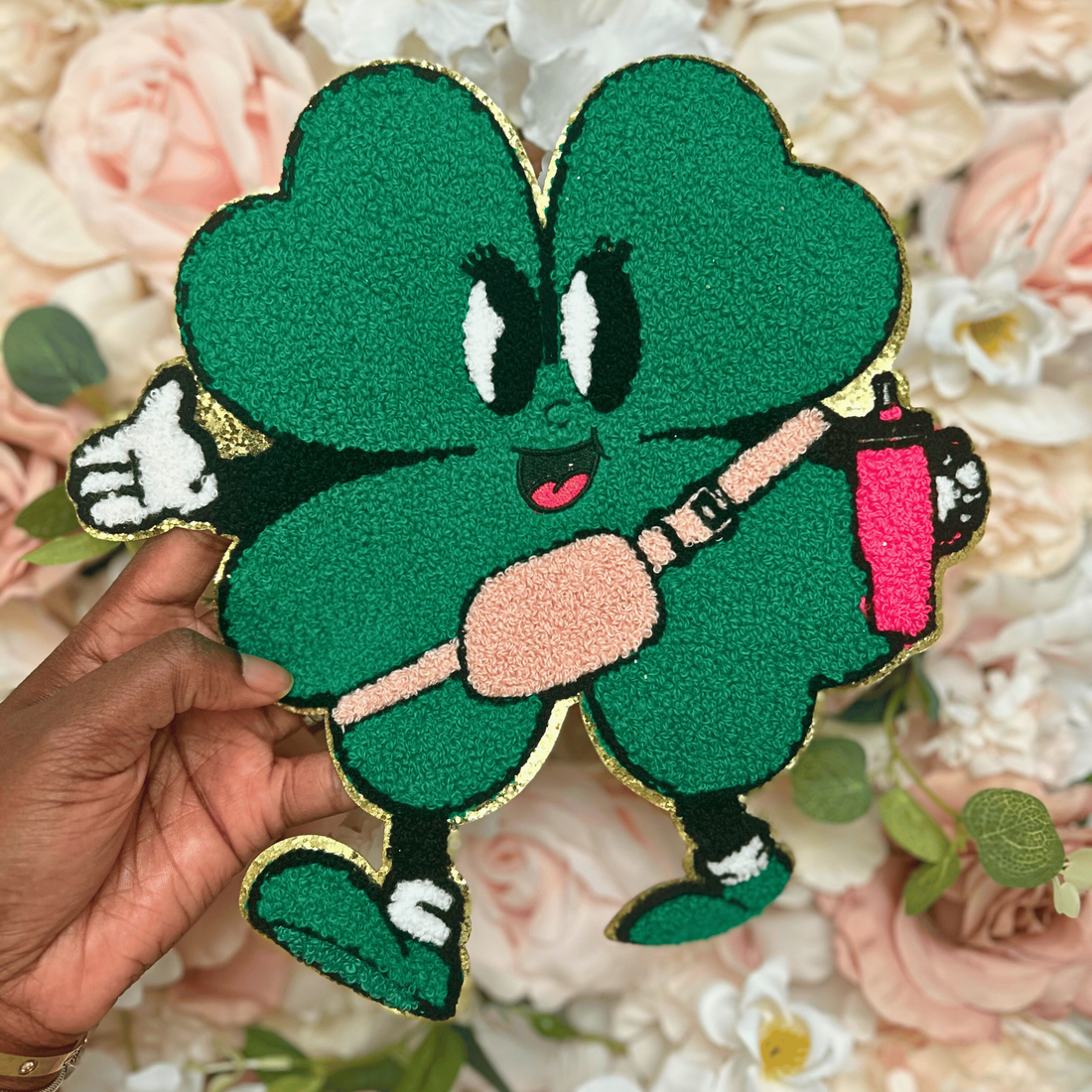 Green cartoon character patch held over a floral background