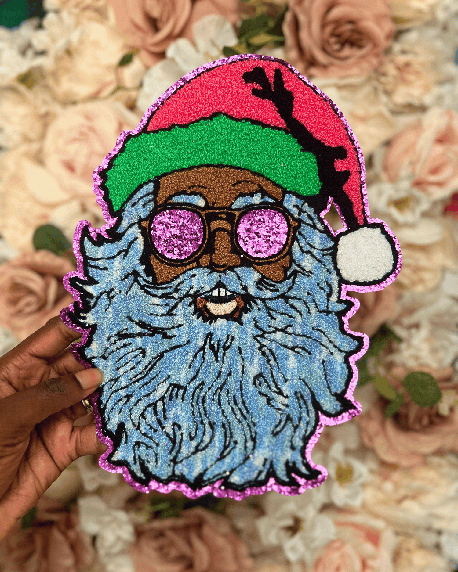 Colorful patch of a bearded figure with glasses and a red hat held over a floral background