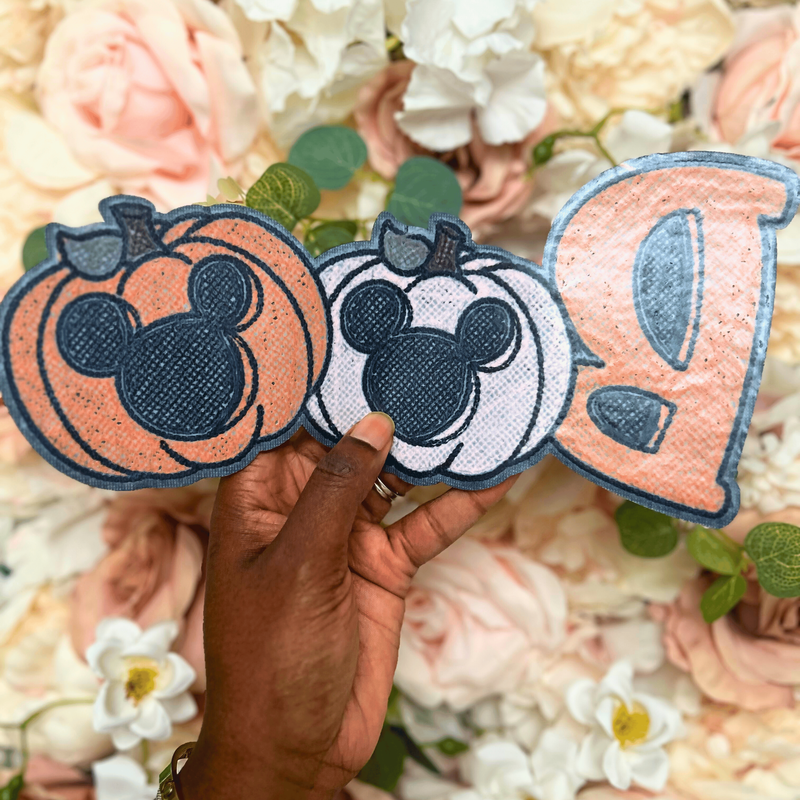 Three decorative patches featuring Mickey Mouse designs held against a floral background.