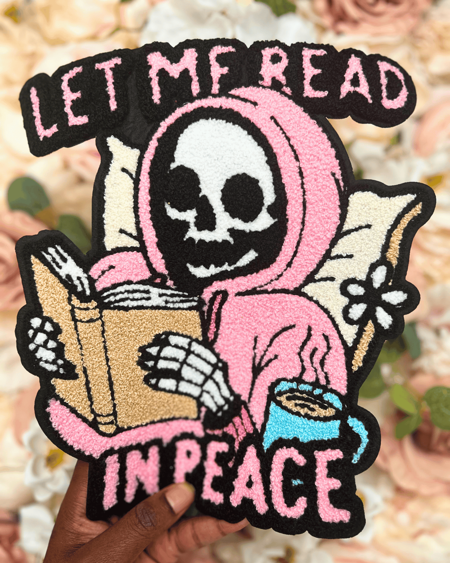 Patch with a skeleton in a pink hood reading a book and holding a coffee cup, with text &