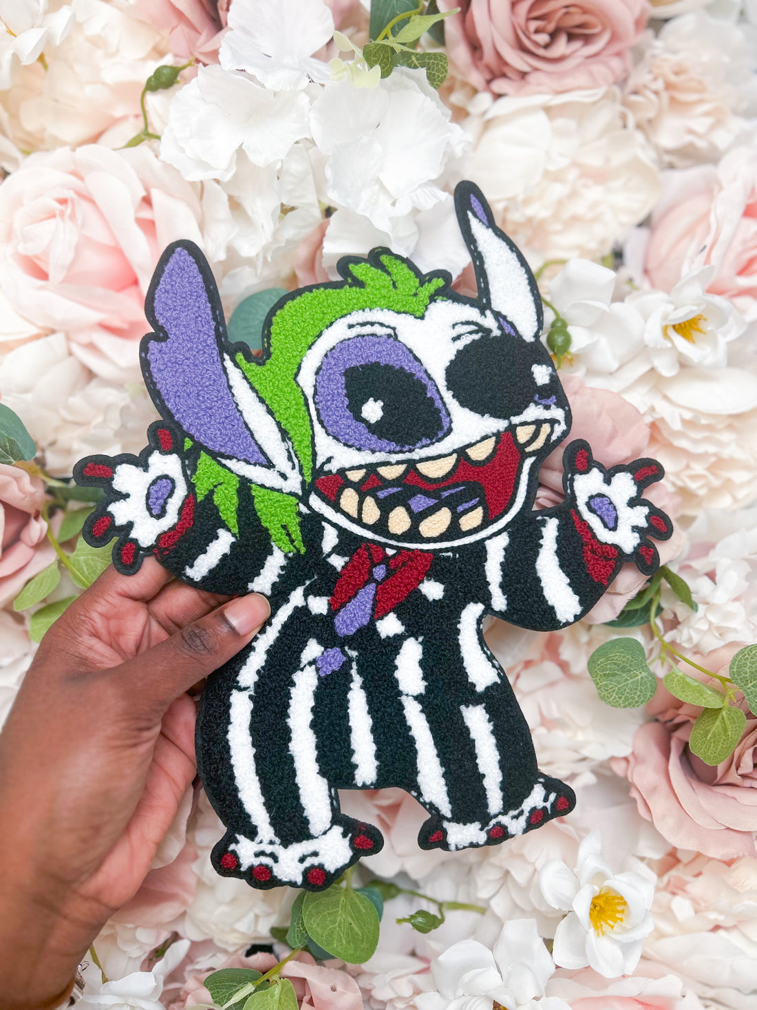 Stitch plush toy with colorful design held over a floral background